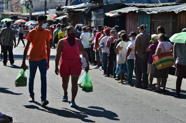 People walk with their buy as other queue at the crowded El Mayoreo market in Tegucigalpa on March 23, 2020 despite an 'absolute curfew' ordered by the Honduran government to slow the spread of the new coronavirus, COVID-19. - Days ago, the government decreed 'an absolute curfew' to force the population to isolate themselves in their homes and curb the spread of the virus in the poor Central American country (Photo by Orlando SIERRA / AFP)