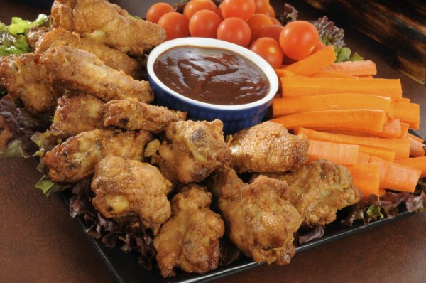 A snack tray with buffalo wings, carrot sticks and cherry tomatoes