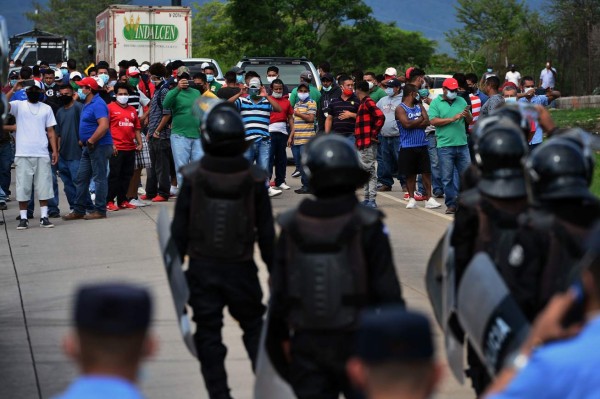 Riot police stand in front of public transport workers who block a highway in demand of aid from the government during a lockdown imposed against the spread of the new coronavirus, 5 km south of Tegucigalpa, on May 21, 2020. - Drivers and conductors assure they have not been able to work in the last 70 days. Accoring to official reports 3,100 people have been infected and 151 have died from COVID-19 in Honduras so far. (Photo by ORLANDO SIERRA / AFP)