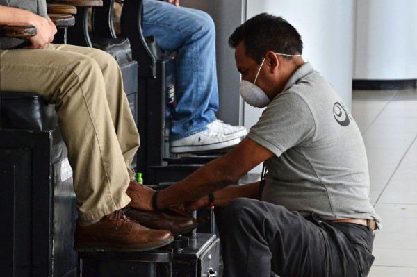 A shoeshiner wears a protective face mask while working to prevent the spread of the new Coronavirus, COVID-19, at Toncontin International Airport, in Tegucigalpa, on March 12, 2020. - Honduran Government has suspended classes at schools and universities. (Photo by ORLANDO SIERRA / AFP)