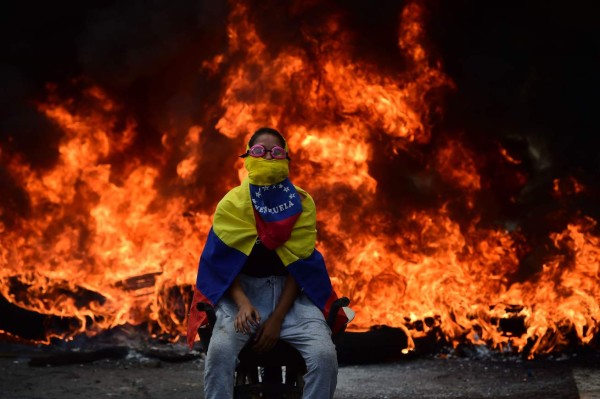 A Venezuelan opposition activist is backdropped by a burning barricade during a demonstration against President Nicolas Maduro in Caracas, on April 24, 2017.Protesters rallied on Monday vowing to block Venezuela's main roads to raise pressure on Maduro after three weeks of deadly unrest that have left 21 people dead. Riot police fired rubber bullets and tear gas to break up one of the first rallies in eastern Caracas early Monday while other groups were gathering elsewhere, the opposition said. / AFP PHOTO / Ronaldo SCHEMIDT