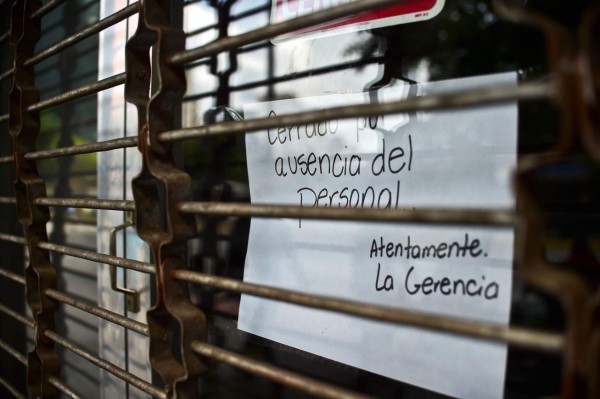 A closed store shows a sign which reads 'closed for lack of staff' in Caracas, on October 28, 2016. Venezuela's opposition sought to pressure President Nicolas Maduro on Friday with a strike, which he threatened to break with army takeovers of paralyzed firms. The strike risks exacerbating the shortages of food and goods gripping the country, but it seemed to be only partially observed on Friday morning. / AFP PHOTO / RONALDO SCHEMIDT