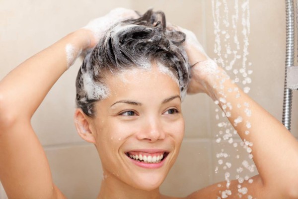 Woman washing hair with shampoo foam in shower smiling happy looking at running warm water. Beautiful mixed race Asian Chinese / Caucasian female model in bathroom.Woman in shower washing hair with shampoo.