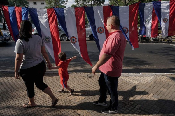 A family walks past Paraguayan flags hanging for sale in downtown Asuncion on April 20, 2018.Paraguay will hold presidential elections on April 22. / AFP PHOTO / EITAN ABRAMOVICH