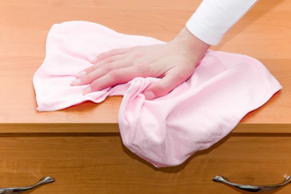 Hand in pink protective glove cleaning wooden furniture with rag. Early spring cleaning or regular clean up. Maid cleans house.