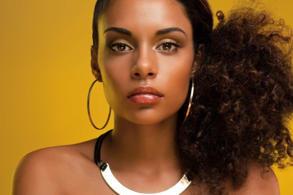 Beautiful African-American woman wearing golden jewelry and posing in front of a yellow background.
