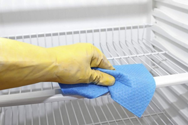 hand with yellow protective glove cleaning refrigerator