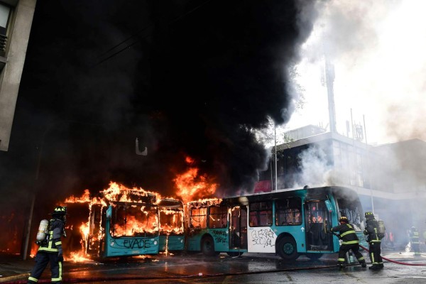 Chilean firefighters extinguish burning buses during clashes between protesters and the riot police in Santiago, on October 19, 2019. - Chile's president declared a state of emergency in Santiago Friday night and gave the military responsibility for security after a day of violent protests over an increase in the price of metro tickets. (Photo by Martin BERNETTI / AFP)