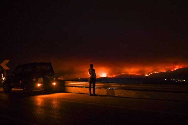 A man stands on the roadside watching a wildfire at Anciao, Leiria, central Portugal, on June 18, 2017. A wildfire in central Portugal killed at least 25 people and injured 16 others, most of them burning to death in their cars, the government said on June 18, 2017. Several hundred firefighters and 160 vehicles were dispatched late on June 17 to tackle the blaze, which broke out in the afternoon in the municipality of Pedrogao Grande before spreading fast across several fronts. / AFP PHOTO / PATRICIA DE MELO MOREIRA