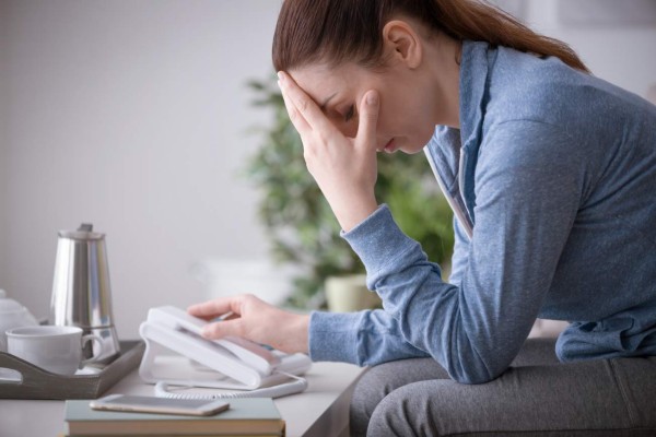 Sad depressed woman at home sitting on the sofa, she is calling an help line with her phone