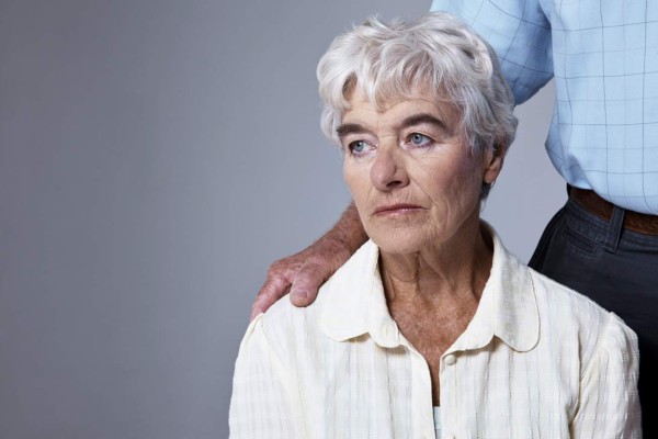 Studio shot of a sad-looking elderly woman with her husband's hand on her shoulder