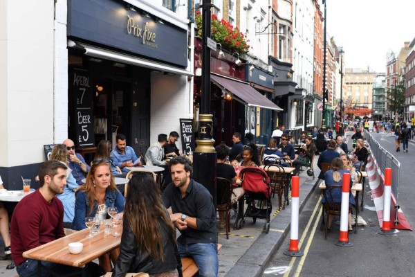 Customers sit outside re-opened bars in Soho in London on July 5, 2020, as the Soho area embraces pedestrianisation in line with an easing of restrictions during the novel coronavirus COVID-19 pandemic. - Pubs in England reopened this weekend for the first time since late March, bringing cheer to drinkers and the industry but fears of public disorder and fresh coronavirus cases. (Photo by DANIEL LEAL-OLIVAS / AFP)
