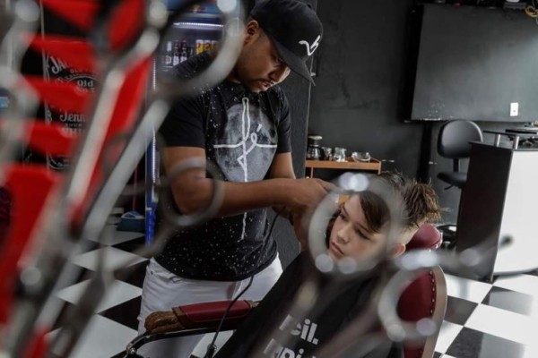 Fotografía fechada el 10 de abril de 2019 que muestra al barbero Ariel Franco, que estuvo en la cárcel dos años, mientras corta el pelo a un niño y aplica su atrevido corte 'blindado', una clase de tupé que no se deshace por días y lleva tintes y diseños de una variada paleta de colores, en una barbería en la Brasilandia, una de las mayores favelas de la capital paulista (Brasil). EFE