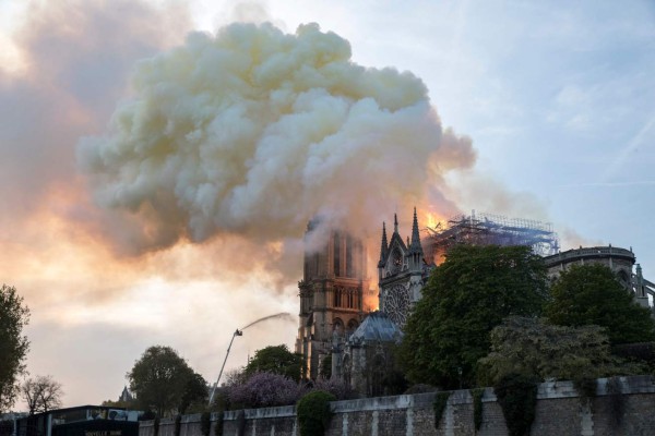 Flames and smoke are seen billowing from the roof at Notre-Dame Cathedral in Paris on April 15, 2019. - A huge fire swept through the roof of the famed Notre-Dame Cathedral in central Paris on April 15, 2019, sending flames and huge clouds of grey smoke billowing into the sky. The flames and smoke plumed from the spire and roof of the gothic cathedral, visited by millions of people a year. A spokesman for the cathedral told AFP that the wooden structure supporting the roof was being gutted by the blaze. (Photo by THOMAS SAMSON / AFP)