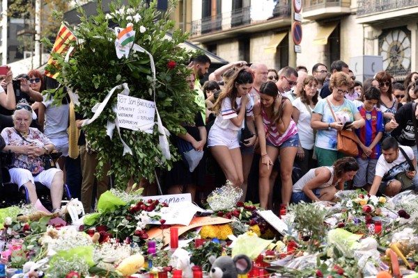 People stand next to flowers, candles and other items set up on the Las Ramblas boulevard in Barcelona as they pay tribute to the victims of the Barcelona attack, three days after a van ploughed into the crowd, killing 13 persons and injuring over 100 on August 20, 2017. Drivers have ploughed on August 17, 2017 into pedestrians in two quick-succession, separate attacks in Barcelona and another popular Spanish seaside city, leaving 14 people dead and injuring more than 100 others. In the first incident, which was claimed by the Islamic State group, a white van sped into a street packed full of tourists in central Barcelona on Thursday afternoon, knocking people out of the way and killing 13 in a scene of chaos and horror. Some eight hours later in Cambrils, a city 120 kilometres south of Barcelona, an Audi A3 car rammed into pedestrians, injuring six civilians -- one of them critical -- and a police officer, authorities said. / AFP PHOTO / JAVIER SORIANO