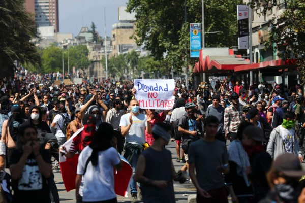 People protest with a sign reading 'Dignity, not military men' in Santiago, on October 20, 2019. - Fresh clashes broke out in Chile's capital Santiago on Sunday after two people died when a supermarket was torched overnight as violent protests sparked by anger over economic conditions and social inequality raged into a third day. (Photo by Pablo VERA / AFP)