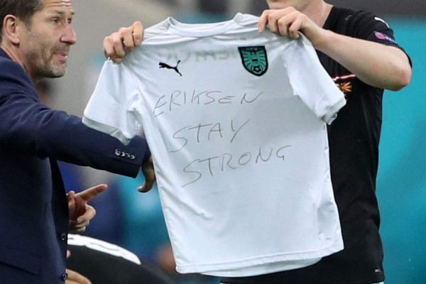 Austria's forward Michael Gregoritsch holds a t-shirt reading 'Eriksen, stay strong', in reference to Denmark's midfielder Christian Eriksen who collapsed yesterday on the pitch, as he celebrates after scoring his team's second goal during the UEFA EURO 2020 Group C football match between Austria and North Macedonia at the National Arena in Bucharest on June 13, 2021. (Photo by MARKO DJURICA / various sources / AFP)