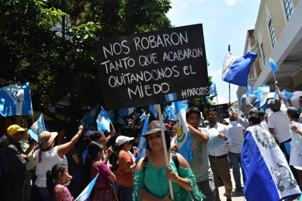 People hold a sign reading Hunger and death during a protest in demand of the resignation of Guatemalan President Alejandro Giammattei, at Constitution Square in Guatemala City on August 22, 2020, amid the COVID-19 coronavirus pandemic. (Photo by Carlos ALONZO / AFP)