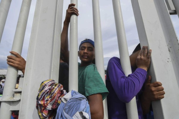 Honduran migrants heading in a caravan to de US, are pictured through a border fence on the Guatemala-Mexico international bridge in Ciudad Hidalgo, Chiapas state, Mexico, on October 19, 2018. - Honduran migrants who have made their way through Central America were gathering at Guatemala's northern border with Mexico on Friday, despite President Donald Trump's threat to deploy the military to stop them entering the United States. (Photo by AFP)