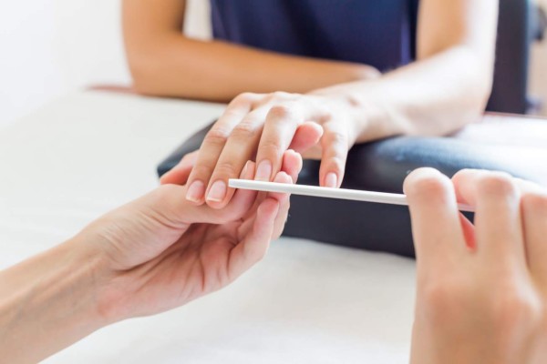 Manicurist performing a professional manicure in a beauty salon shaping and filing a clients fingernails with a nail file, close up view of their hands