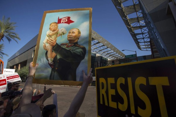 PHOENIX, AZ - AUGUST 22: A protester holds a painting depicting President Donald Trump and Russian President Vladimir Putin outside the Phoenix Convention Center where a rally by Trump was being held on August 22, 2017 in Phoenix, Arizona. An earlier statement by the president that he was considering a pardon for Joe Arpaio,, the former sheriff of Maricopa County who was convicted of criminal contempt of court for defying a court order in a case involving racial profiling, has angered Latinos and immigrant rights advocates. David McNew/Getty Images/AFP