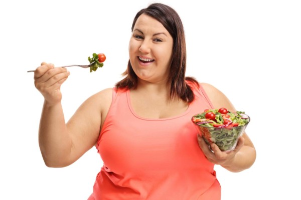 Overweight woman eating a salad isolated on white background