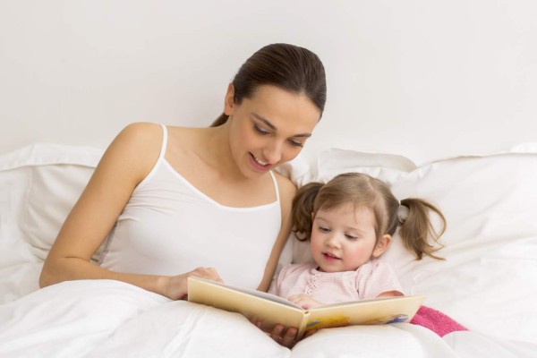 Little girl reading a book with her mother in white bedroom