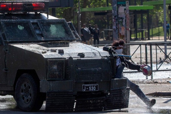 A demonstrator hangs from a riot police vehicle during protests in Santiago, on October 20, 2019. - Fresh clashes broke out in Chile's capital Santiago on Sunday after two people died when a supermarket was torched overnight as violent protests sparked by anger over economic conditions and social inequality raged into a third day. (Photo by CLAUDIO REYES / AFP)