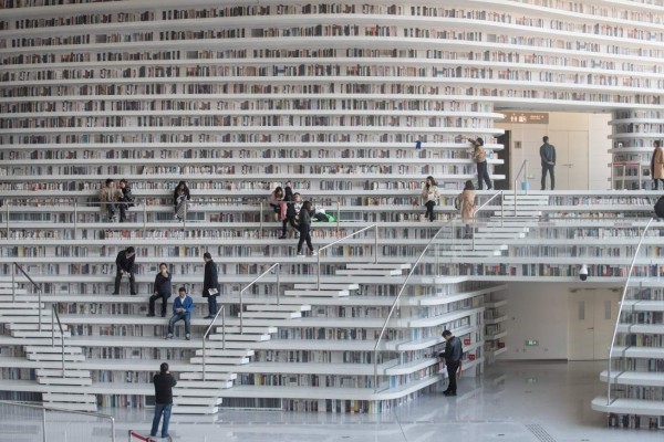 This picture taken on November 14, 2017 shows people visiting the Tianjin Binhai Library.A futuristic Chinese library has wowed book lovers around the world with its white, undulating shelves rising from floor to ceiling, but if you read between the lines you'll spot one problem. Those rows upon rows of book spines are mostly images printed on the aluminium plates that make up the backs of shelves. / AFP PHOTO / FRED DUFOUR / To go with AFP story China-library-architecture, FOCUS by Becky Davis