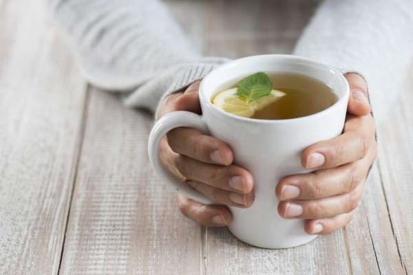 Herbal tea on wood background. Woman holding mug.