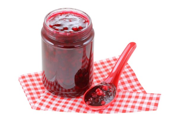 A spoon next to a jar of Cranberry jam isolated on white background
