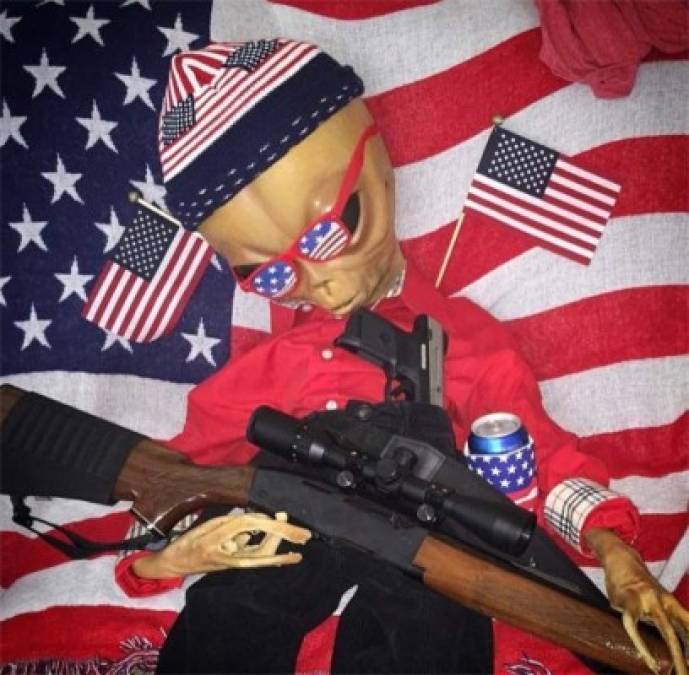 El alien rodeado de banderas estadounidenses y con un arma.