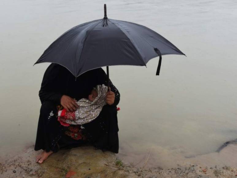 BANGLADÉS. Exiliados en el fango. Una mujer rohinyá se cubre de la lluvia mientras carga a su hijo en un campamento en Bangladés; los campos de refugiados se han anegado.