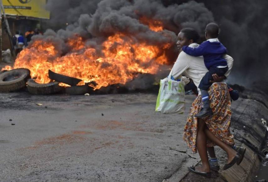 Una mujer carga a un escolar más allá de una barricada ardiendo en Kibera en una manifestación en Kenia.
