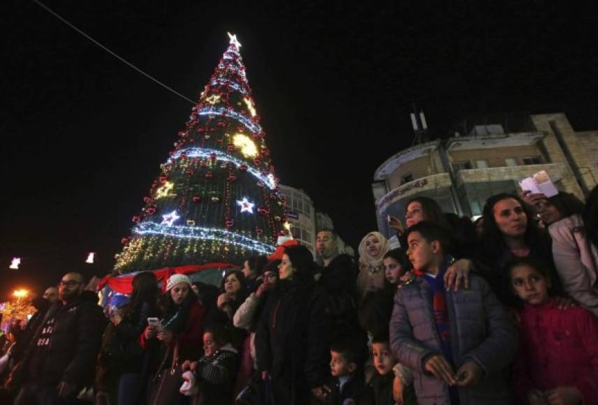 Varias personas observan los participantes de la marcha navideña disfrazados de Papa Noel en Ramala, Palestina.