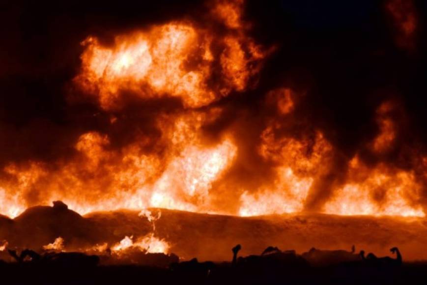 The fire is raging behind the bodies of burned victims at the scene of a massive blaze trigerred by a leaky pipeline in Tlahuelilpan, Hidalgo state, Mexico on January 18, 2019. - An explosion and fire has killed at least 66 people who were collecting fuel gushing from a leaking pipeline in central Mexico, the Hidalgo state governor said on Saturday. (Photo by FRANCISCO VILLEDA / AFP)