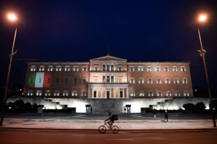 Italia es uno de los países más afectados por la pandemia. Como una muestrra de solidaridad, una bandera italiana se refleja sobre la fachada del parlamento griego en Atenas.