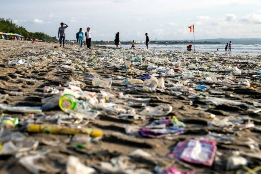Indonesia. <br/>Playa inundada por basura plástica. Personas caminan por la playa junto a restos de plástico que llegó a la costa traído por las olas en la playa de Kuta, el destino turístico más conocido de la isla de Bali.