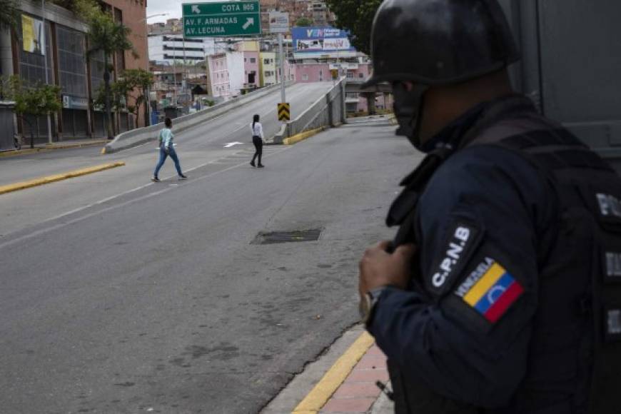 A member of the Bolivarian National Police observes two women crossing an empty avenue during clashes between police and alleged members of a criminal gang in the surroundings of La Cota 905 neighborhood in Caracas, on July 8, 2021. - A new clash between police and criminal gangs has been taking place in the Venezuelan capital since Wednesday, resulting in at least four deaths, most of them from stray bullets, according to local media. (Photo by Yuri CORTEZ / AFP)