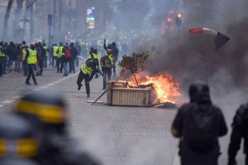 Protestors wearing 'Yellow vests' (gilets jaunes) clash with riot police amid tear gas near the Champs Elysees in Paris on December 8, 2018 during a protest of against rising costs of living they blame on high taxes. - Paris was on high alert on December 8 with major security measures in place ahead of fresh 'yellow vest' protests which authorities fear could turn violent for a second weekend in a row. (Photo by Lucas BARIOULET / AFP)