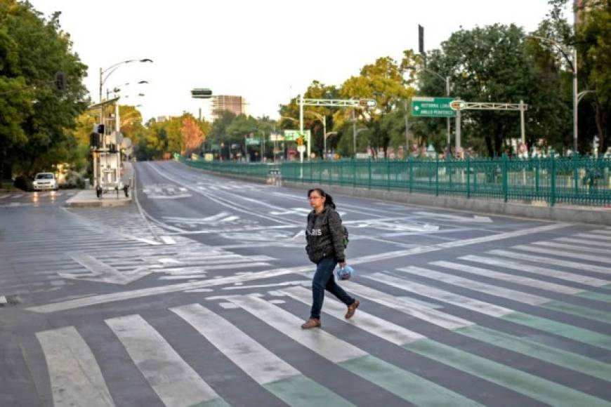 Una mujer cruza hoy una calle casi vacía en la Ciudad de México durante el brote del nuevo coronavirus COVID-19. / AFP