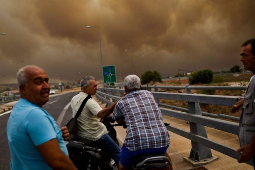 People look the smoke from a bridge as a wildfire burns in Kineta, near Athens, on July 23, 2018. / AFP PHOTO / ANGELOS TZORTZINIS