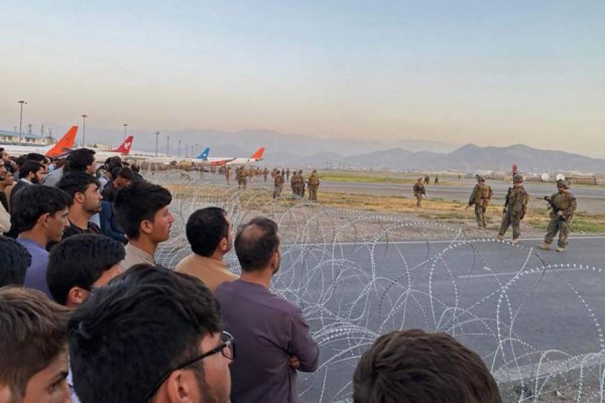Afghans (L) crowd at the airport as US soldiers stand guard in Kabul on August 16, 2021. (Photo by Shakib Rahmani / AFP)