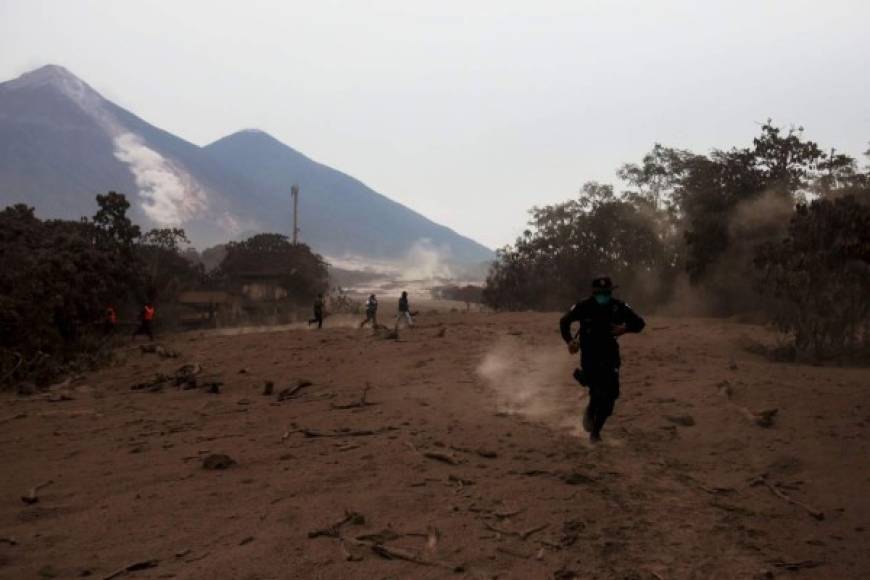 -FOTODELDIA- GU1005. ESCUINTLA (GUATEMALA), 04/06/2018.- Un policía corre por un deslizamiento de fluido del volcán de Fuego hoy, lunes 4 de junio de 2018, después de la erupción, en el Caserío San Miguel Los Lotes, Escuintla (Guatemala). La cifra de heridos por la erupción del volcán de Fuego en Guatemala aumento de 20 a 46 y la de muertos se mantiene en 25, informaron las autoridades que al amanecer de hoy reanudaron las labores de búsqueda de desaparecidos EFE/Esteban Biba