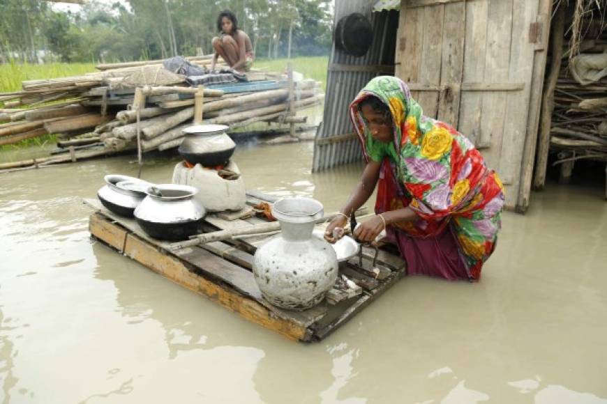 BANGLADESH. En crisis por las lluvias. Una mujer cocina frente a su casa inundada en Mainkdir, Bogra, un tercio del territorio del país está anegado.