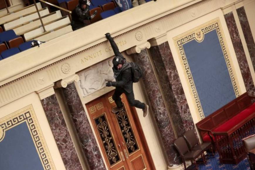 TOPSHOT - WASHINGTON, DC - JANUARY 06: A protester is seen hanging from the balcony in the Senate Chamber on January 06, 2021 in Washington, DC. Congress held a joint session today to ratify President-elect Joe Biden's 306-232 Electoral College win over President Donald Trump. Pro-Trump protesters have entered the U.S. Capitol building after mass demonstrations in the nation's capital. Win McNamee/Getty Images/AFP (Photo by WIN MCNAMEE / GETTY IMAGES NORTH AMERICA / AFP)