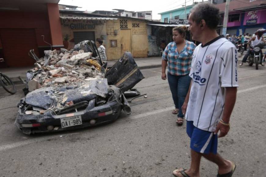 TOPSHOT - People walk past a car squashed by rubble after a 7.8-magnitude quake in Portoviejo, Ecuador on April 17, 2016. <br/>At least 77 people were killed when a powerful earthquake struck Ecuador, destroying buildings and a bridge and sending terrified residents scrambling from their homes, authorities said Sunday. / AFP PHOTO / JUAN CEVALLOS
