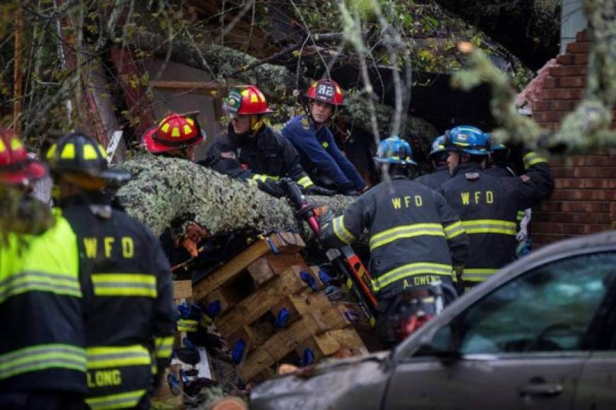 Bomberos trabajan para quitar un árbol que cayó en el techo de una casa y dejó a dos personas heridas.