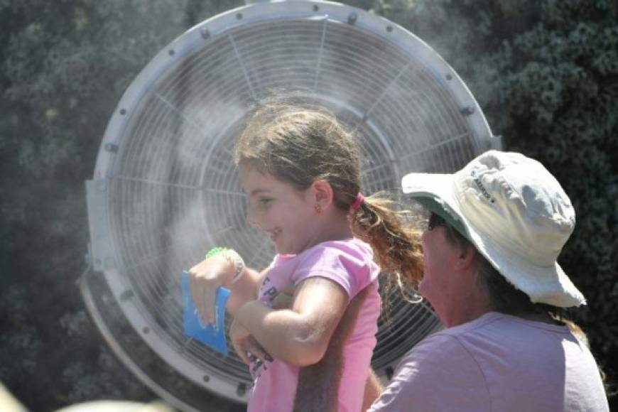 A child is carried in front of a mist fan to cool down from the heat on day one of the Australian Open tennis tournament in Melbourne on January 14, 2019. (Photo by SAEED KHAN / AFP) / -- IMAGE RESTRICTED TO EDITORIAL USE - STRICTLY NO COMMERCIAL USE --