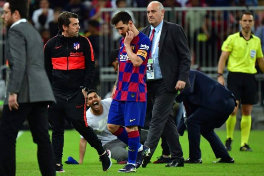 Messi se marchó cabizbajo rumbo al camerino al final del partido, mientras al fondo los miembros de seguridad detienen al aficionado que saltó al campo.